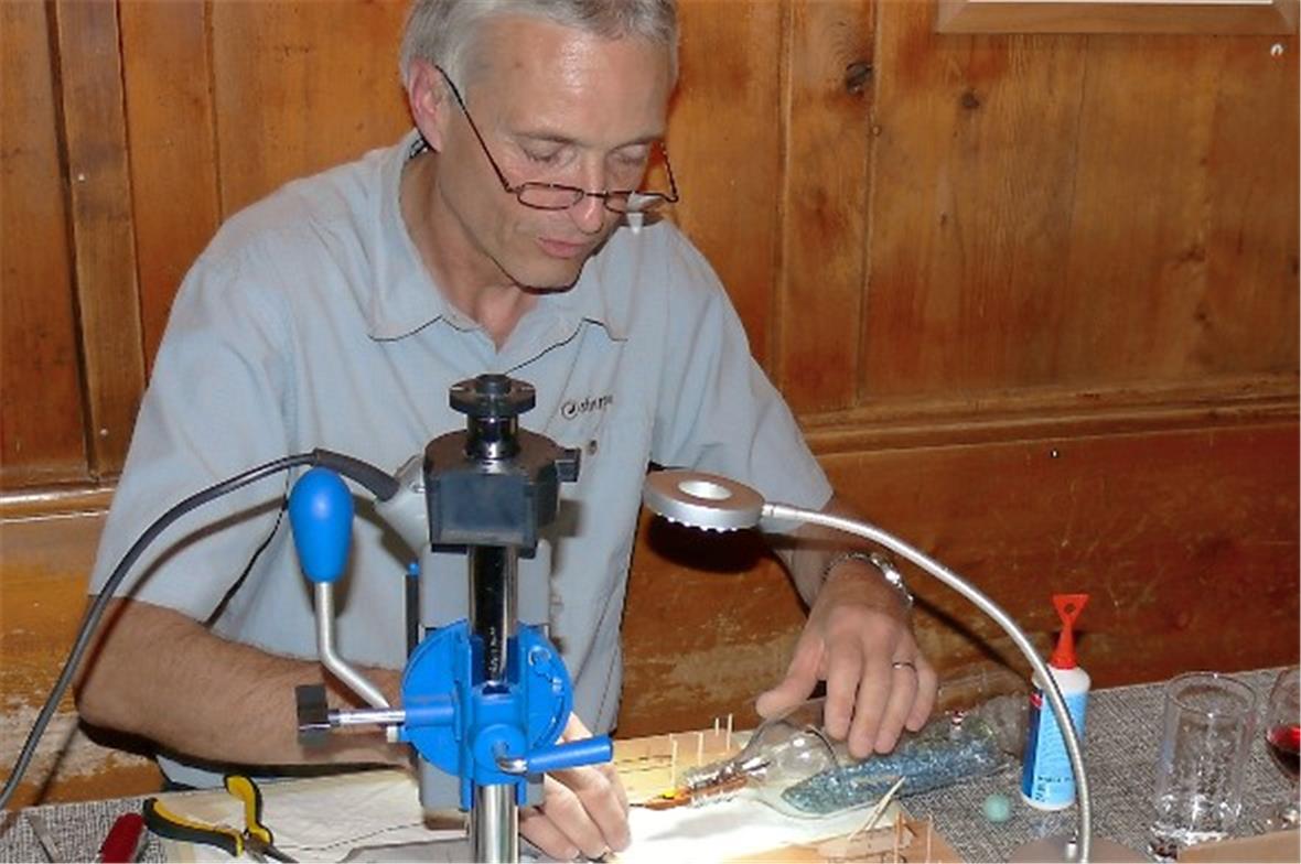 Danach schiebt er das noch gefaltete Schiff in die Flasche.