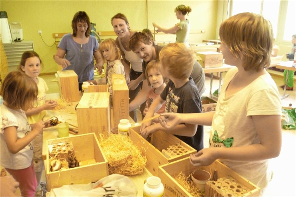 Die drei Leitenden mit einigen Kindern an einem der Werktische.