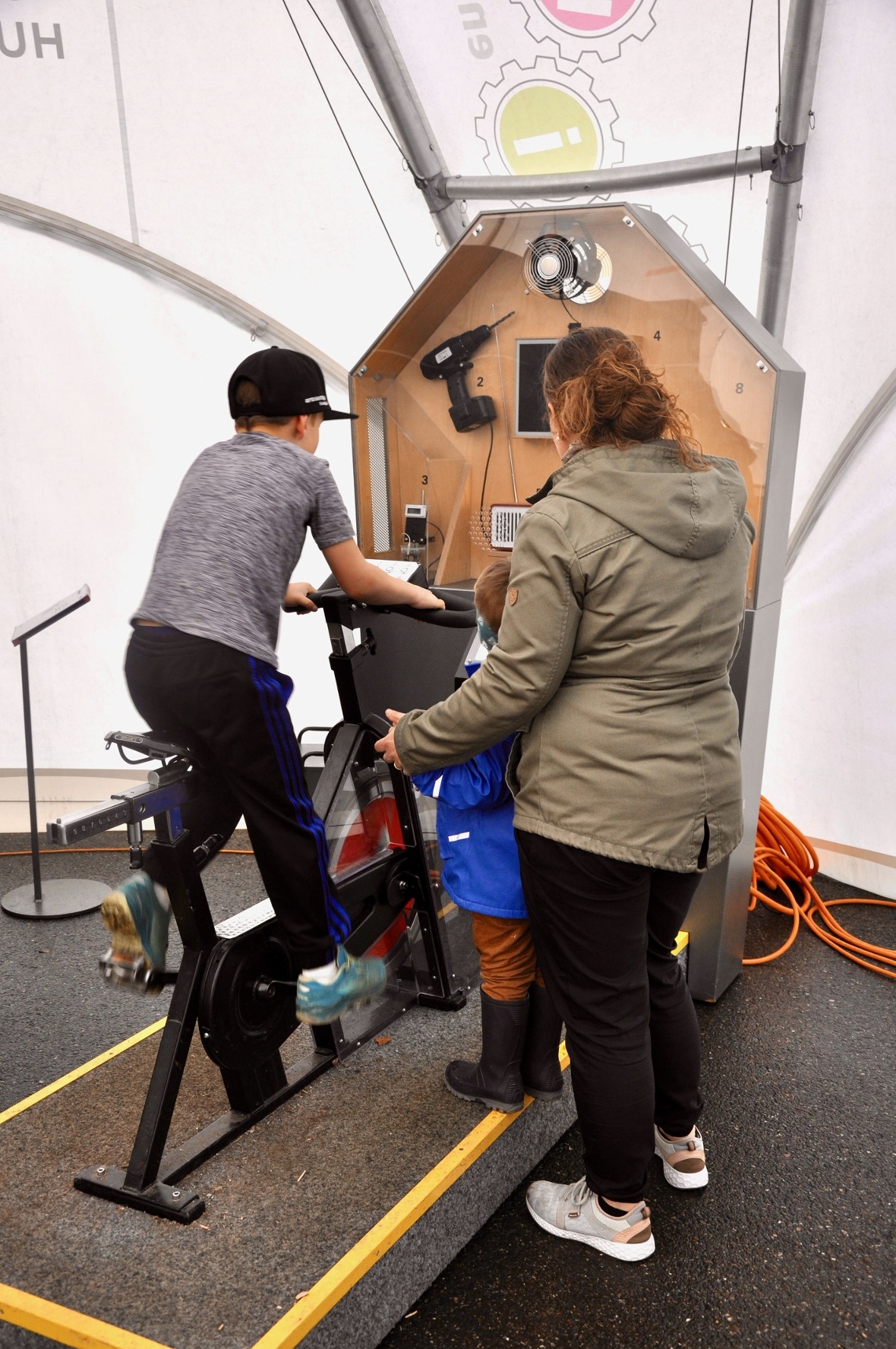 Ein Schüler zeigt seiner Mutter, wie aus Bewegungsenergie elektrische Energie wi...