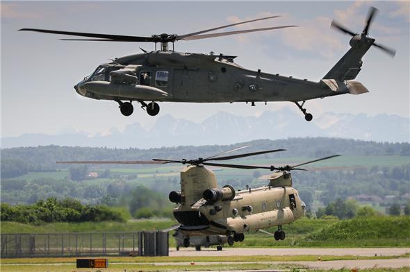 Ein UH-60 «Blackhawk» schwebt über dem Flugplatz Payerne, im Hintergrund setzt ein CH-47 «Chinook» auf dem Boden auf.