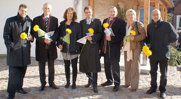 Eine Chrysantheme (mit angehängtem Volksschul-Leitbild) für die gutgelaunten Mitglieder der Bernischen Kantonsregierung: Andreas Rickenbacher, Bernhard Pulver (Regierungspräsident), Barbara Egger-Jenzer, Hans Jürg Käser, Philippe Perrenoud, Beatrice Simon und Staatsschreiber Dr. Kurt Nuspliger vor dem Beinhaus bei der Kirche in Zweisimmen (Regierungsrat Christoph Neuhaus fehlte krankheitshalber).