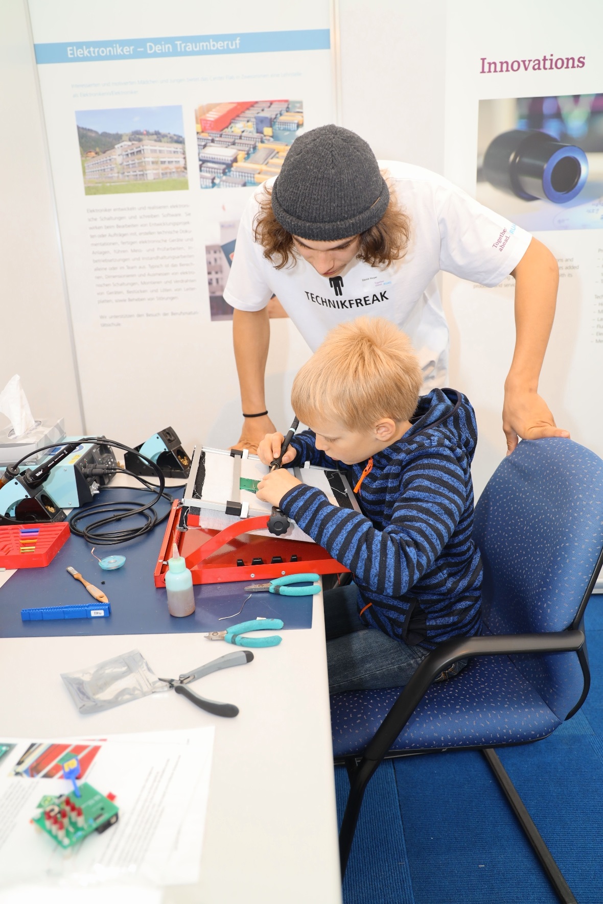 Elektroniker Lehrling bringt begeistertem Schüler das Löten bei.