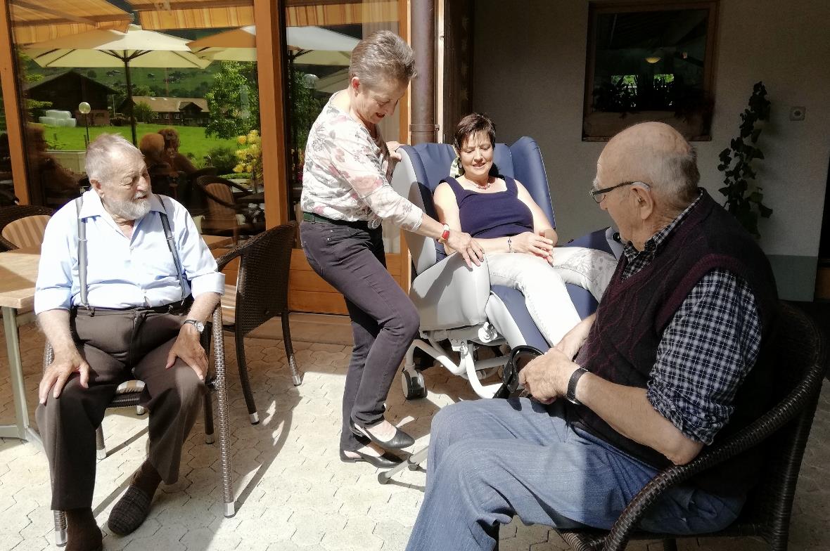 Frau Toscana und Präsidentin Vreni Schletti bei der Vorführung des Pflegestuhl unter kritischen Blicken der Bewohner.