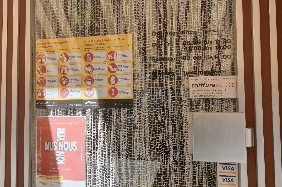 Hinweise zu den aktuellen Schutzmassnahmen an der Tür eines Coiffeursalons.