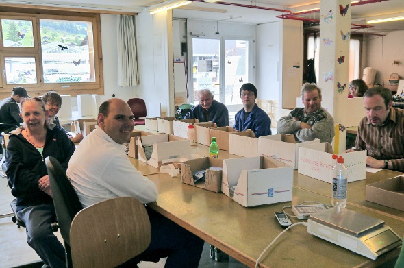 Mitarbeiterinnen und Mitarbeiter der Behindertenwerkstätte in Zweisimmen arbeiten an einem Verpackungsauftrag für Lenk Simmental Tourismus.