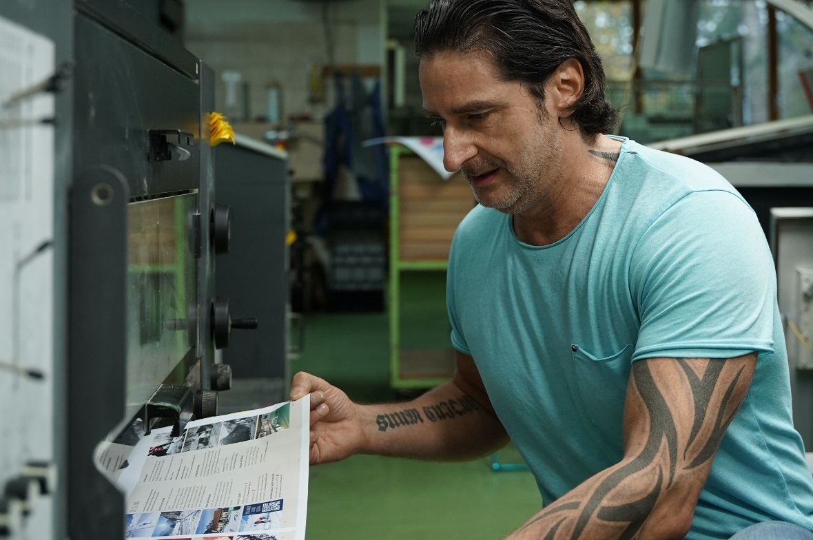 Offsetdrucker Mirko Herrmann nimmt einen bedruckten Bogen zur Qualitätskontrolle aus der Druckmaschine.