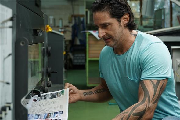 Offsetdrucker Mirko Herrmann nimmt einen bedruckten Bogen zur Qualitätskontrolle aus der Druckmaschine.