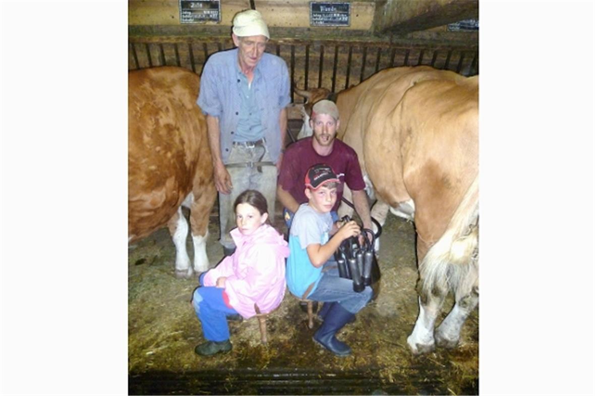 Vater und Sohn Walter und Michael Guggisberg instruieren zwei Kinder an der Melk...